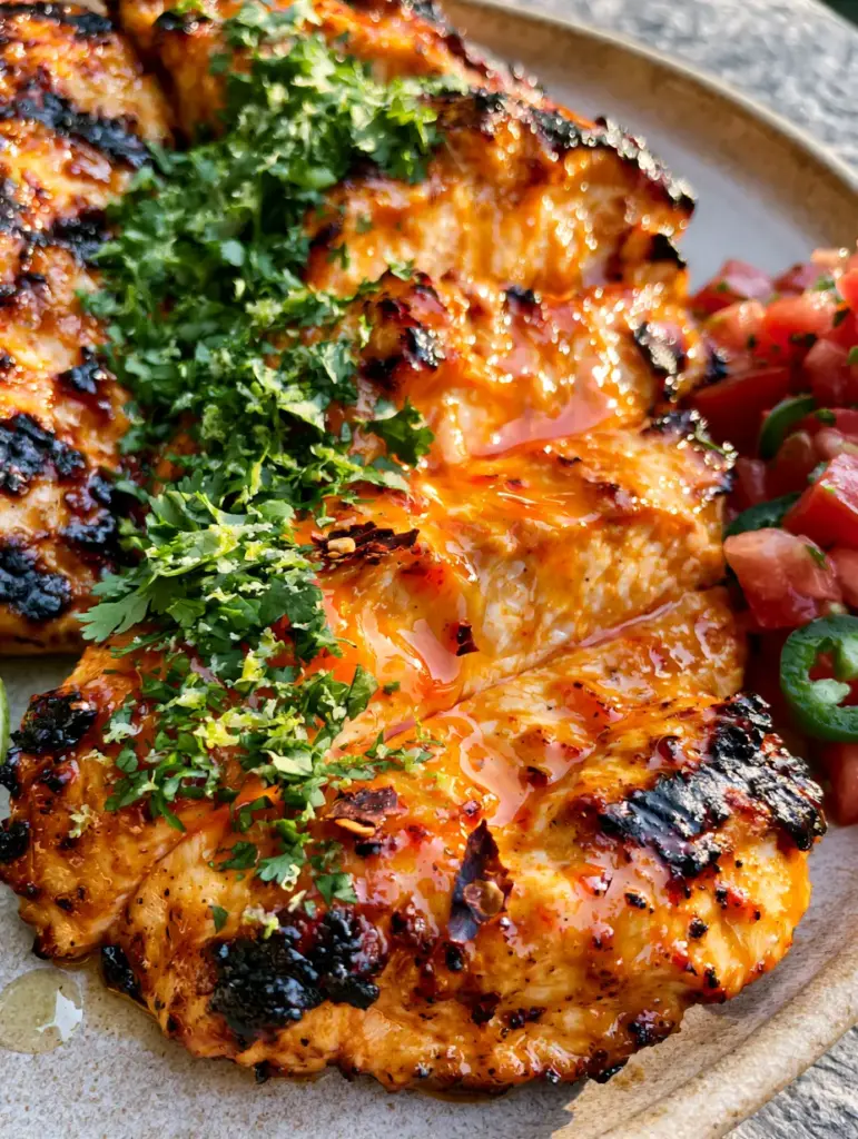 High-angle shot of Mexican chicken marinade grilled chicken with a side of diced tomatoes and jalapeños.