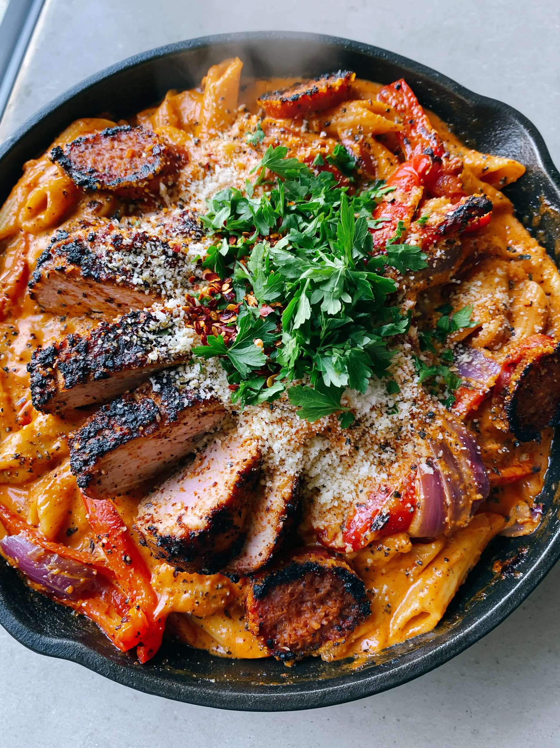 Close up of glossy Creamy Cajun Pasta with visible flecks of black pepper and melted parmesan shavings.