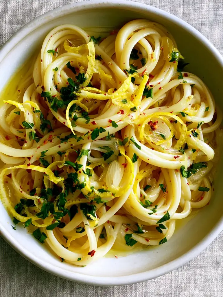 Silky pasta strands with translucent garlic slivers and bright green parsley in a handcrafted bowl.