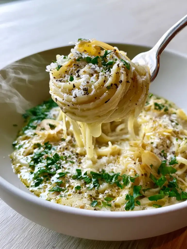 Top-down view of Garlic Butter Pasta with toasted garlic slivers and cracked black pepper on a light wood surface.